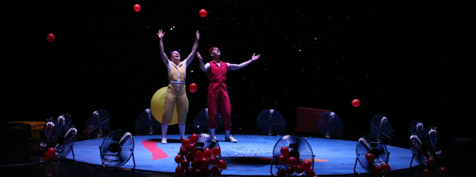 Two people are raising up their hands, surrounded by fans and balloons.