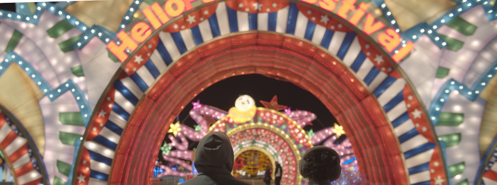 Two people staring at a decorative entrance that says “hello” and “festival” over the opening.