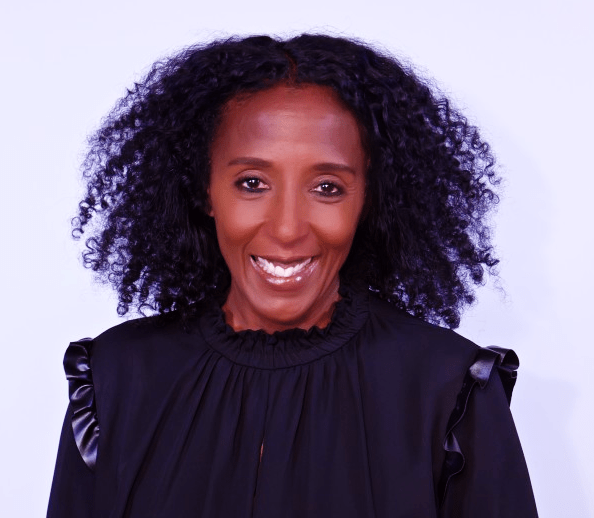 Smiling woman with curly black hair, wearing a black jacket and looking directly at the camera.