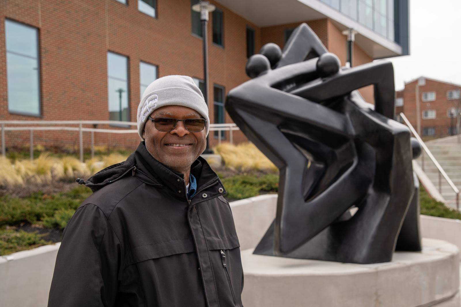 Artist Nnamdi Okonkwo standing next to metal sculpture Community of Stars